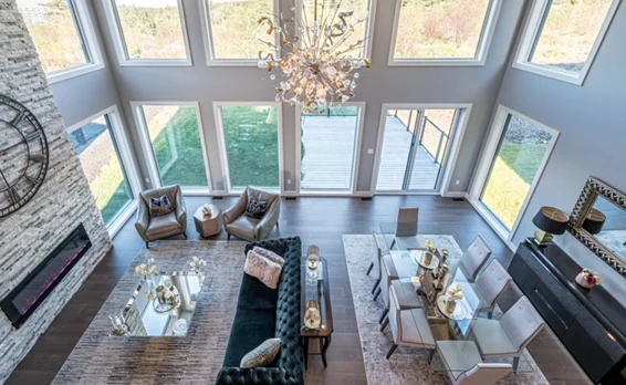 Double-height Halifax great room with a stone fireplace, a wall of windows and layered seating, designed by MAD Design Interiors