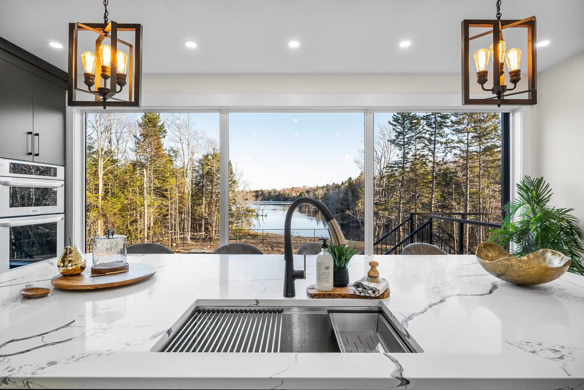 A marble kitchen island with a black faucet, facing a wall of windows overlooking a lake in Halifax, designed by MAD Design Interiors